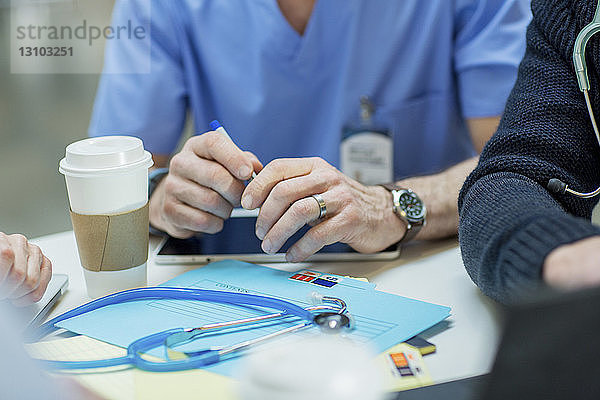 Abgetrennte Hand eines Arztes mit einem Kollegen  der im Krankenhaus am Tisch sitzt