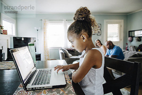 Seitenansicht eines Mädchens  das einen Laptop benutzt  während die Eltern im Hintergrund sitzen