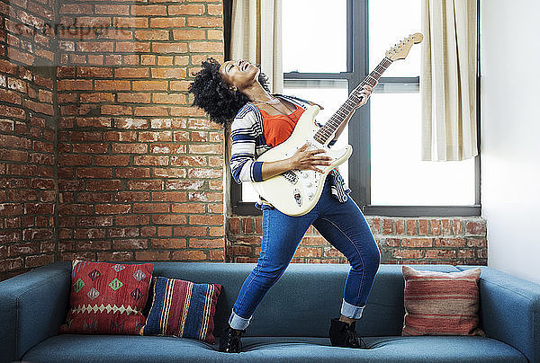 Glückliche Frau singt beim Gitarrenspiel auf dem Sofa