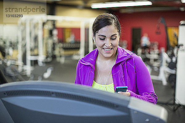 Lächelnde Frau hört Musik  während sie im Fitnessstudio auf dem Laufband trainiert