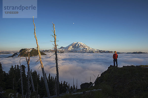 Rückansicht eines männlichen Wanderers  der bei Sonnenaufgang auf einem Berg durch eine Wolkenlandschaft steht