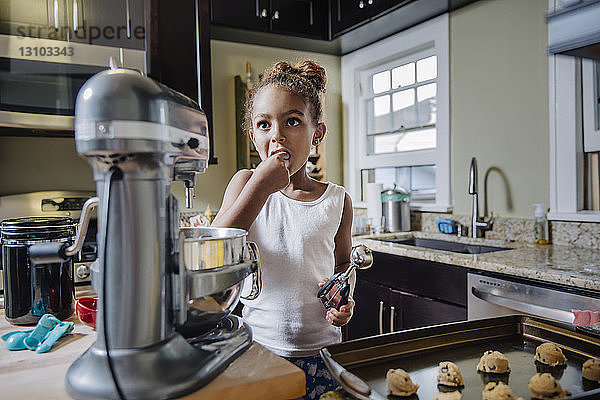 Süßes Mädchen isst  während es in der Küche Schokokekse zubereitet
