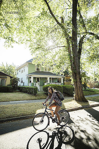 Frau in voller Länge mit dem Fahrrad auf der Straße gegen Häuser gefahren