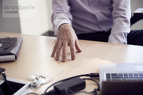 Mittelteil eines Geschäftsmannes mit Laptop-Computer auf dem Schreibtisch sitzend im Büro