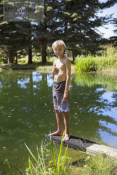 Porträt eines Jungen  der auf einem Sprungbrett am Seeufer steht