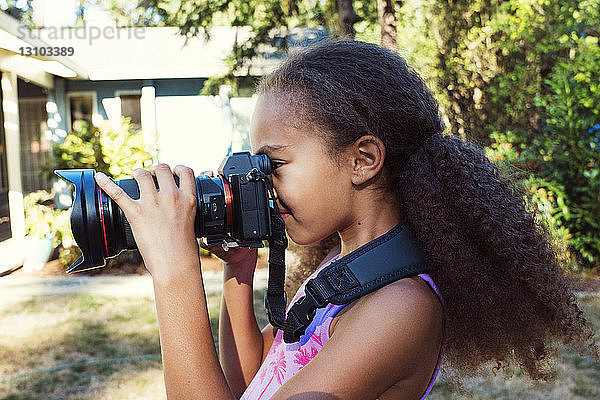 Seitenansicht eines Mädchens  das im Hof stehend mit einer Digitalkamera fotografiert