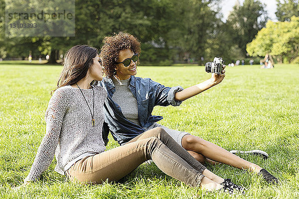 Freunde fotografieren  während sie im Park auf dem Feld sitzen