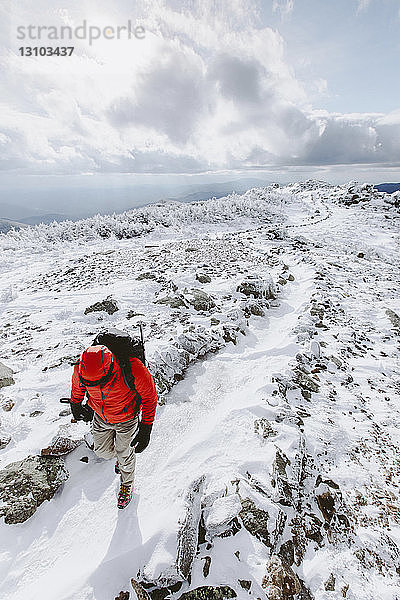 Hochwinkelaufnahme eines Rucksacktouristen in warmer Kleidung  der im Winter auf Schnee läuft