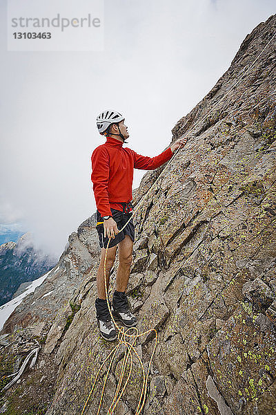 Wanderer in voller Länge mit Seil beim Klettern in Felsformationen gegen Wolken