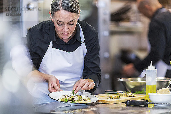 Köchin garniert Essen  während eine Mitarbeiterin im Hintergrund im Restaurant arbeitet