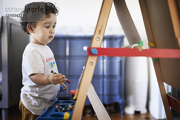 Süßer kleiner Junge hält Buntstift  während er zu Hause an der Leinwand steht