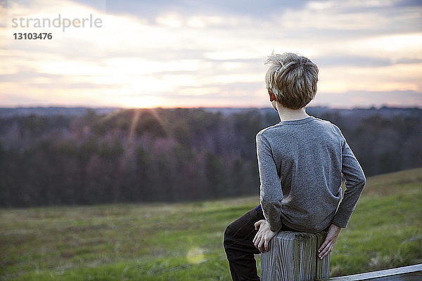 Junge sieht Sonnenuntergang auf dem Zaun sitzend