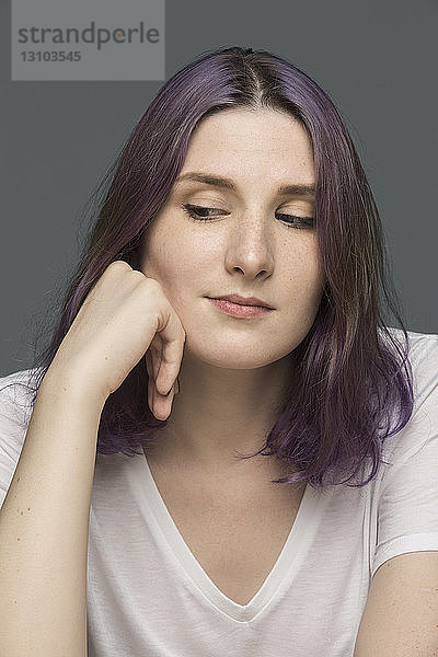 Porträt einer jungen Frau mit gefärbtem Haar und Blick nach unten vor grauem Hintergrund