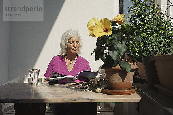 Ältere Frau liest Zeitschrift auf sonniger Terrasse