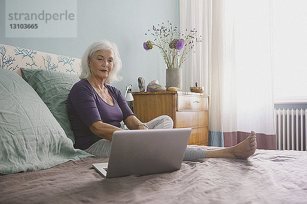 Ältere Frau mit Laptop auf dem Bett