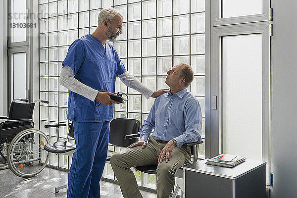 Männlicher Arzt spricht mit einem Patienten im Wartezimmer einer Klinik und tröstet ihn