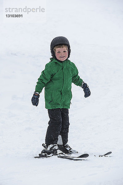 Porträt lächelnder  süßer Junge beim Skifahren im Schnee