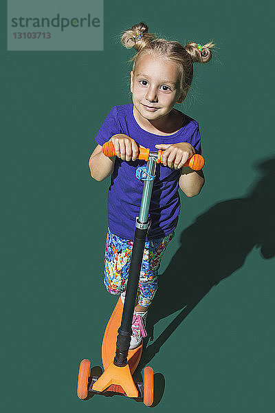 Porträt selbstbewusstes Mädchen fährt Roller gegen grünen Hintergrund