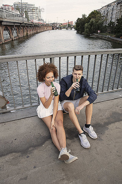 Junges Paar trinkt Bier auf einer städtischen Brücke über einen Fluss