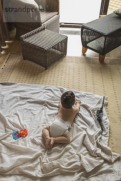 Ein kleiner Junge liegt auf einer Decke im Wohnzimmer