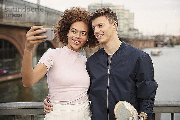 Junges Paar mit Smartphone nimmt Selfie auf Brücke