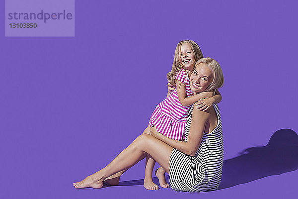 Porträt lächelnd Mutter und Tochter in gestreiften Kleidern umarmt gegen lila Hintergrund