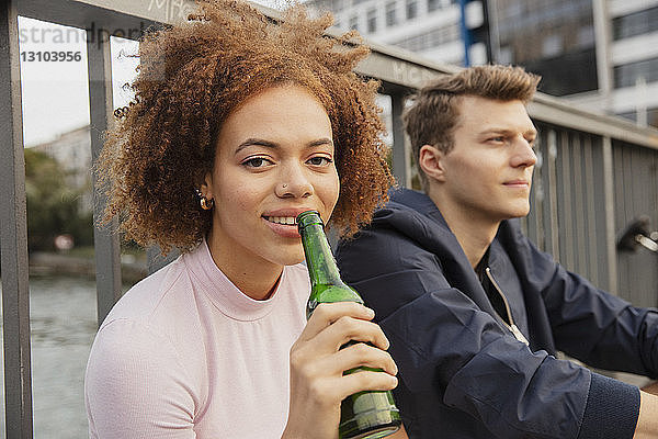 Porträt junge Frau trinkt Bier auf städtischer Brücke