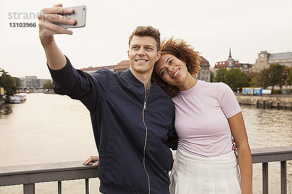 Zärtliches junges Paar mit Smartphone nimmt Selfie auf städtischen Brücke