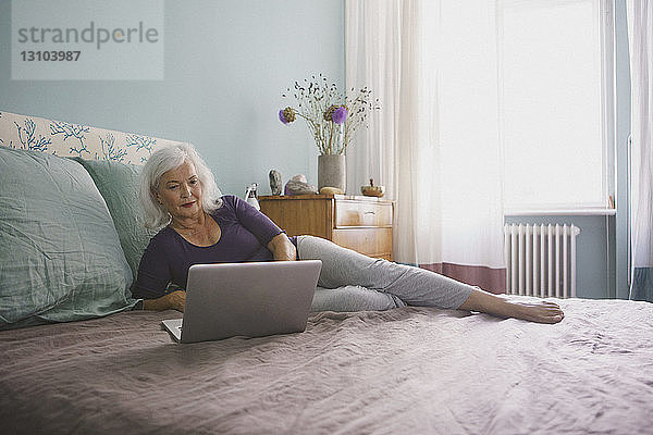 Ältere Frau mit Laptop auf dem Bett