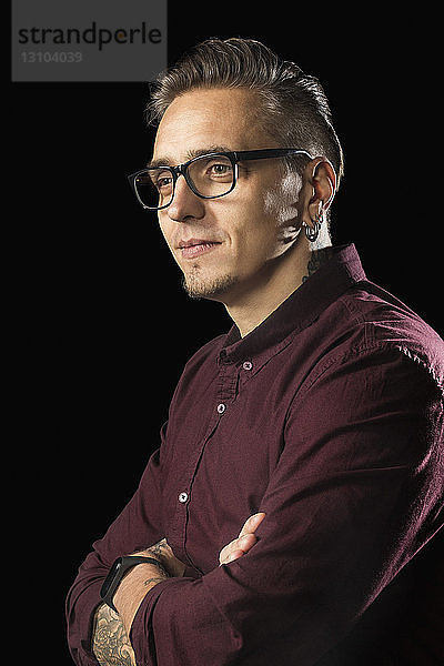 Porträt eines Mannes mit Brille und verschränkten Armen vor schwarzem Hintergrund