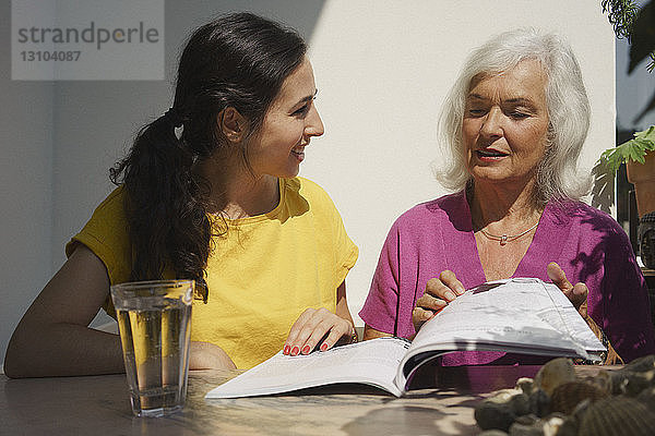 Ältere Mutter und Tochter lesen eine Zeitschrift auf einer sonnigen Terrasse