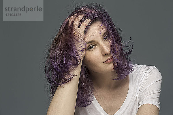 Porträt einer selbstbewussten jungen Frau mit gefärbtem und zerzaustem Haar vor grauem Hintergrund