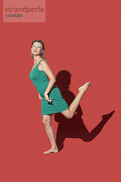 Porträt selbstbewusste  barfuß lebende Frau auf rotem Hintergrund