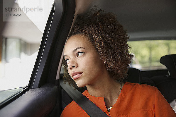 Nachdenkliche junge Frau  die im Auto sitzt und aus dem Fenster schaut