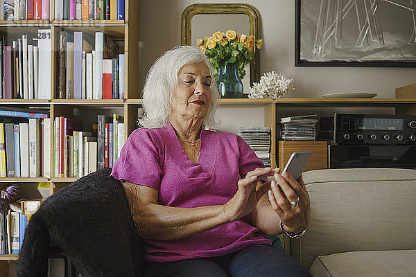 Ältere Frau benutzt ihr Smartphone auf dem Wohnzimmersofa
