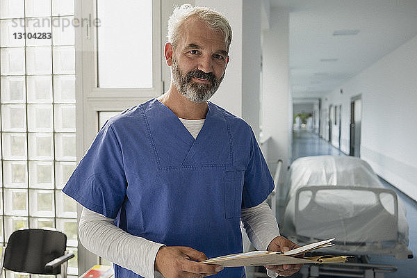 Porträt selbstbewusster männlicher Arzt mit Krankenblatt in einem Krankenhauskorridor