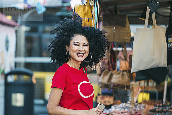 Porträt einer lächelnden  selbstbewussten jungen Frau beim Einkaufen an einem Marktstand