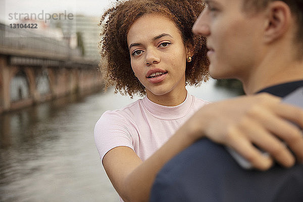 Porträt einer jungen Frau  die ihren Freund am Flussufer umarmt