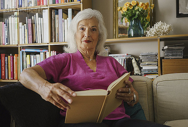 Porträt einer selbstbewussten älteren Frau  die im Wohnzimmer ein Buch liest