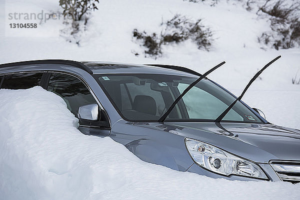 Im Schnee geparktes Auto mit eingeschalteten Scheibenwischern