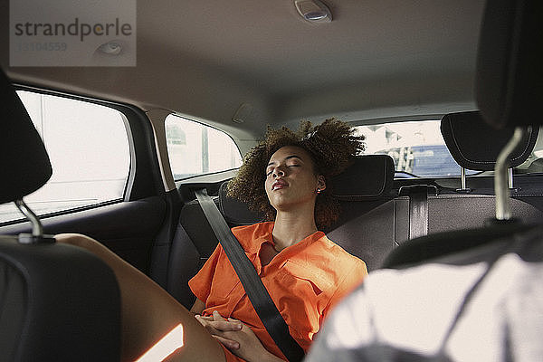 Müde junge Frau schläft auf dem Rücksitz eines Autos