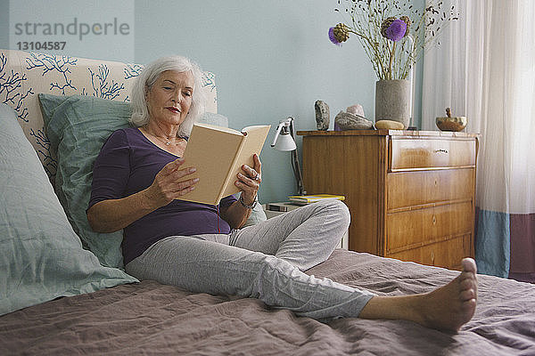 Ältere Frau liest Buch auf dem Bett