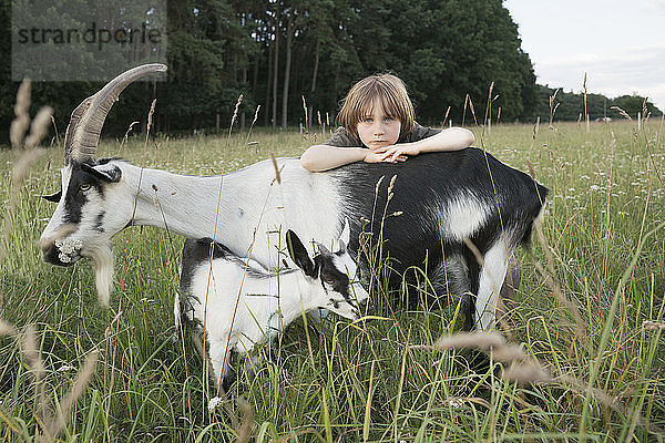 Porträt eines Mädchens  das sich auf eine Ziege in einem ländlichen Feld stützt