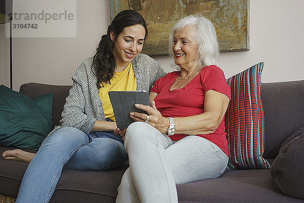 Ältere Mutter und Tochter benutzen ein digitales Tablet auf dem Wohnzimmersofa