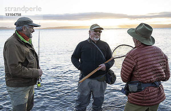 Zwei Fliegenfischer sprechen mit ihrem Führer über neue Techniken beim Fliegenfischen auf Cutthroat-Forellen an einem Strand an der Nordwestküste der USA.