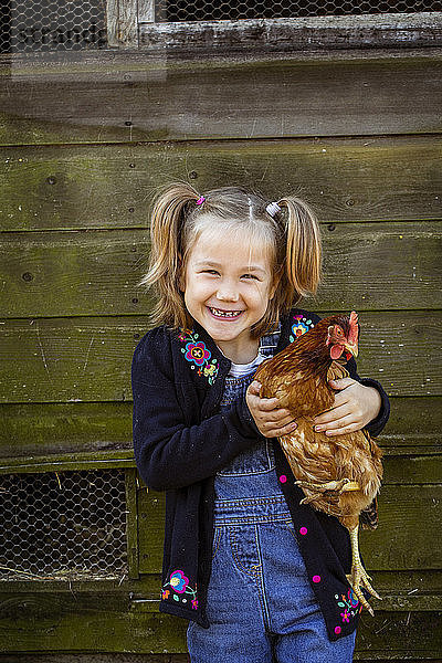 Lächelndes Mädchen hält Hühnchen und schaut in die Kamera.