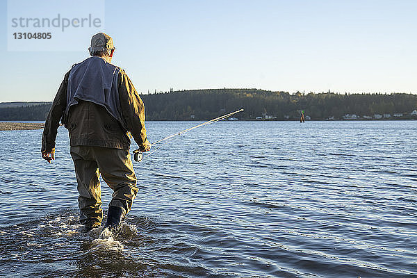 Ein Fliegenfischer  der zu einer neuen Position im flachen Salzwasser geht  während er an der Küste nach Cutthroat-Forellen und Lachsen fischt.