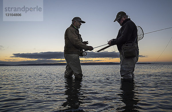 Ein männlicher Fliegenfischer beobachtet  wie sein Führer eine neue Fliege anlegt  um an einem Salzwasserstrand im Fort Flagler State Park im Nordwesten des Bundesstaates Washington  USA  nach Lachsen oder Forellen zu suchen.