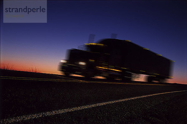 Ein Schlafwagen  der sich bei Sonnenaufgang als Silhouette auf der Straße abzeichnet  ein orangefarbenes Licht am Horizont.