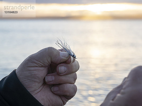 Nahaufnahme eines Fliegenfischers  der eine neue Fliege an seine Schnur bindet  in der Erwartung  eine weitere Forelle oder einen Lachs im Salzwasser zu fangen.